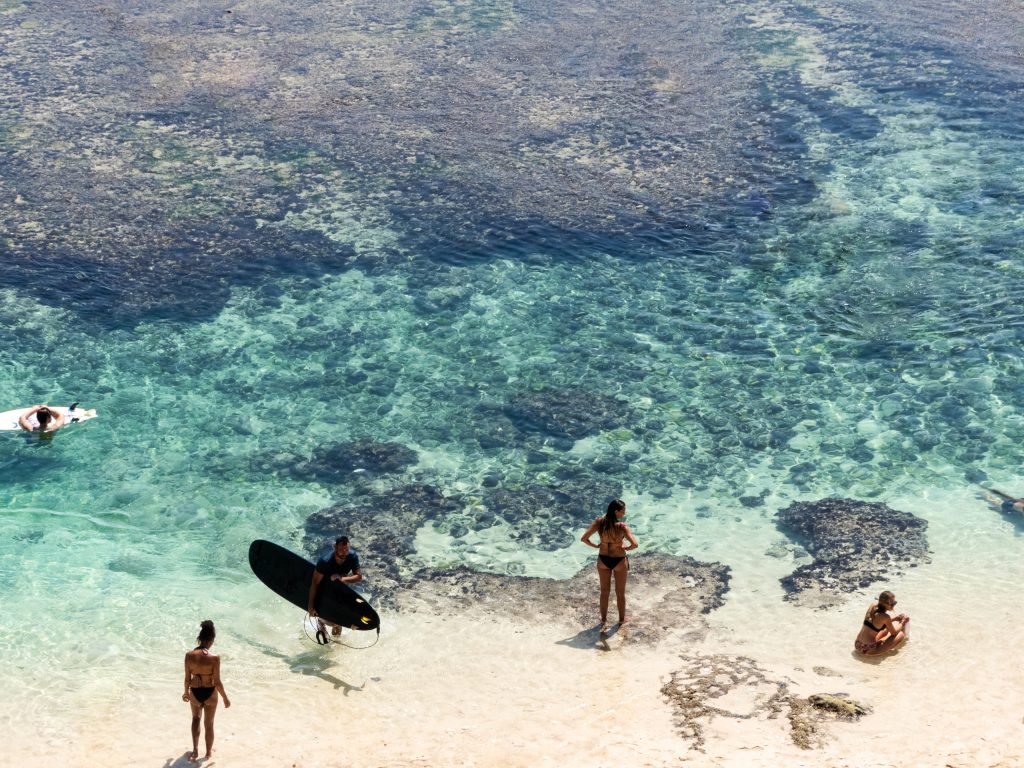 suluban beach surfers in fronnt of blue waters on a uluwatu day trip itinerary