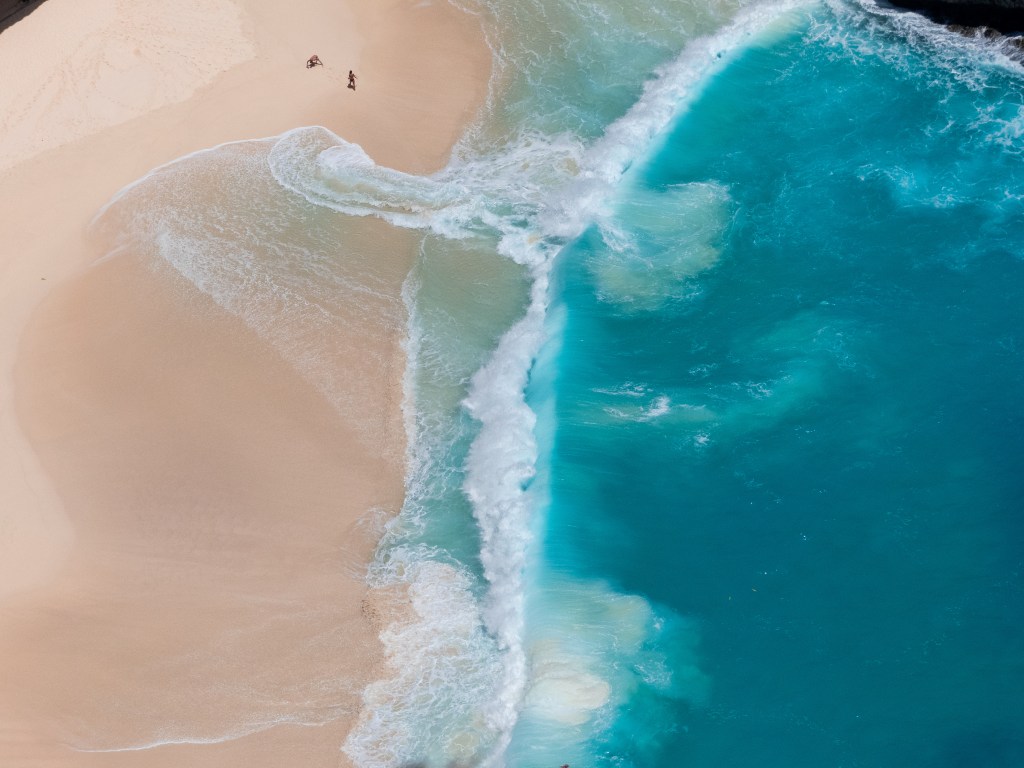 Drone shot people on white sand beach blue waves