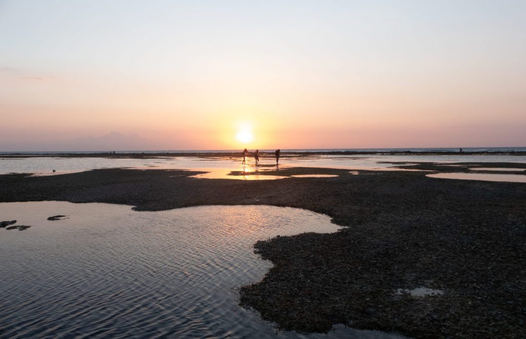 sunset at the beach with tidal pools in gili trawangan and people walking