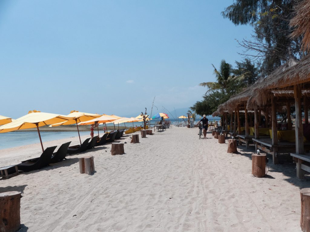 beach road in gili air with sand and yellow umbrellas and beach bars