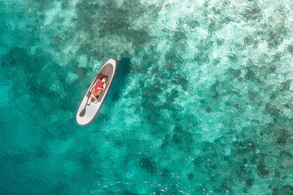 drone shot of girl on paddle board over coral reefs and blue waters