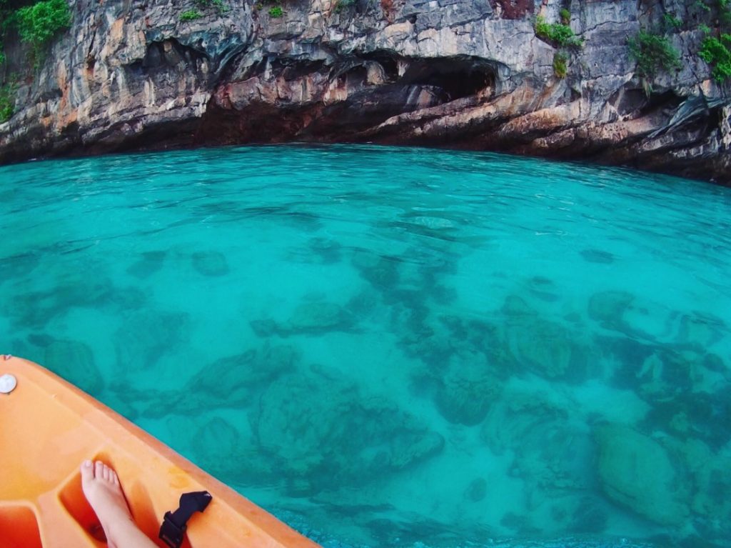 blue ocean water with kayak and feet and rocks in the background at an island in thailand which you can visiting island hopping for your 2-week itinerary