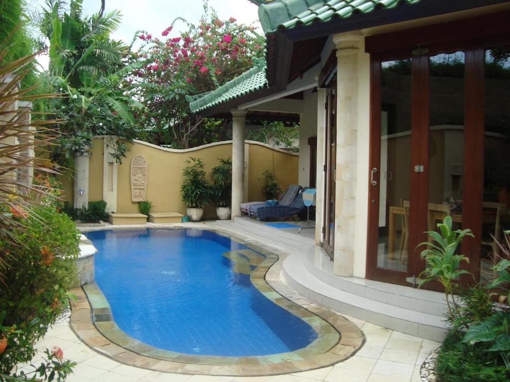 Villa with pool outdoor shower and sunloungers surrounded by trees and flowers 