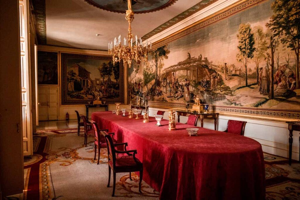 Inside the banquet hall of el escorial with large landscape painting and red tablecloth and chairs