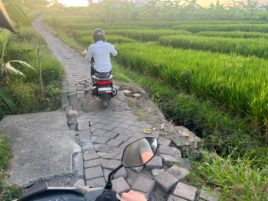 broken street in Bali with green rice field and scooter cobblestones shortcut