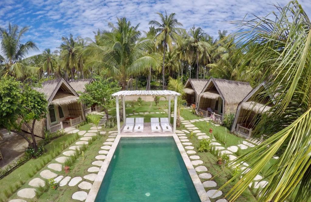 drone shot of villa with pool with sunloungers and huts surrounded by palm trees