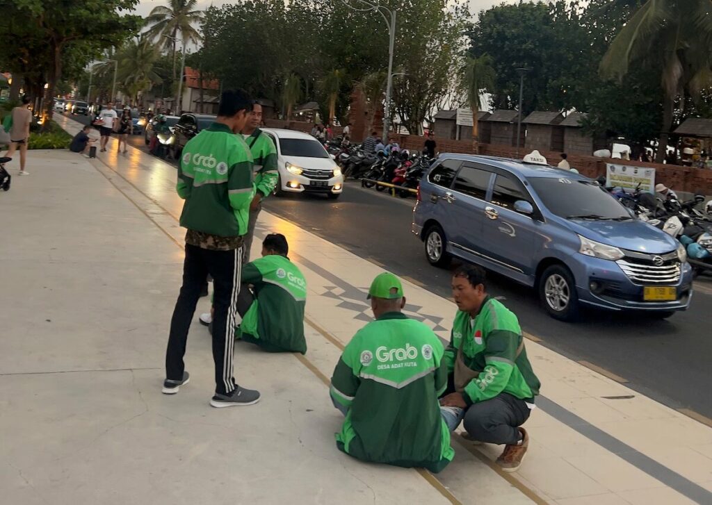 gojek and grab drivers sitting and standing on the stairs in kuta bali waiting